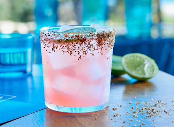 Pale pink margarita in an old fashioned glass with chilli and salt rim against a blue background