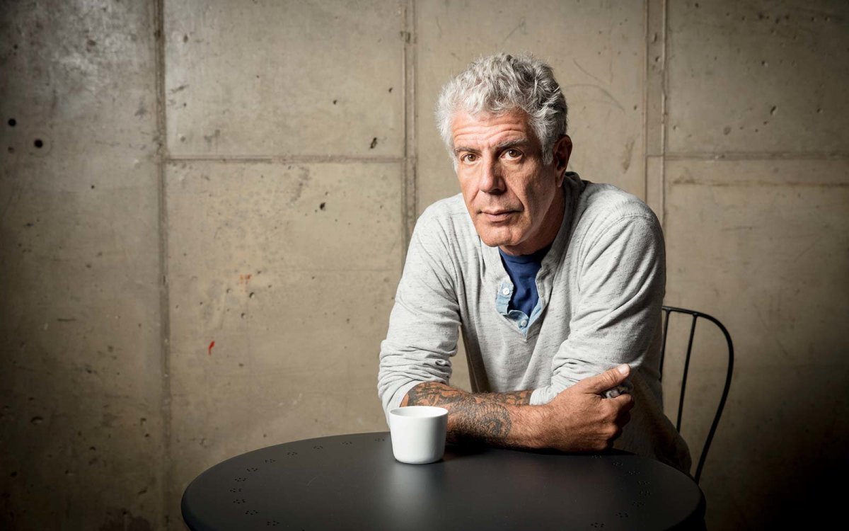 Anthony Bourdain looking at camera, arms folded, leaning on table