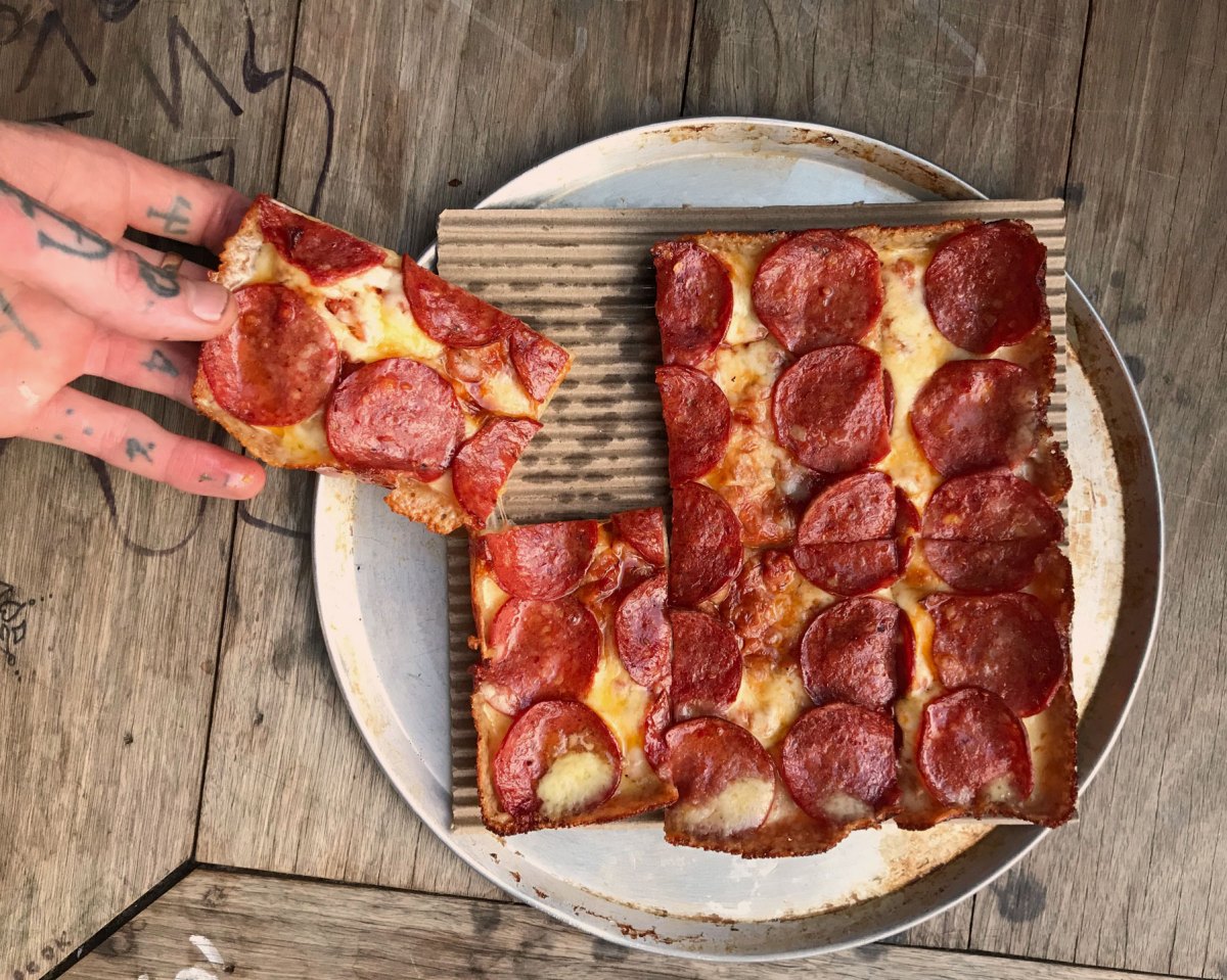 Mary's Detroit style pizza. A square pizza with pepperoni. A hand is pulling a slice away from the plate.